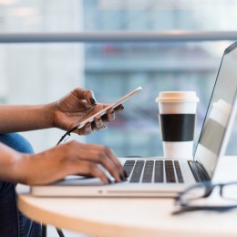 Person working on laptop and holding phone